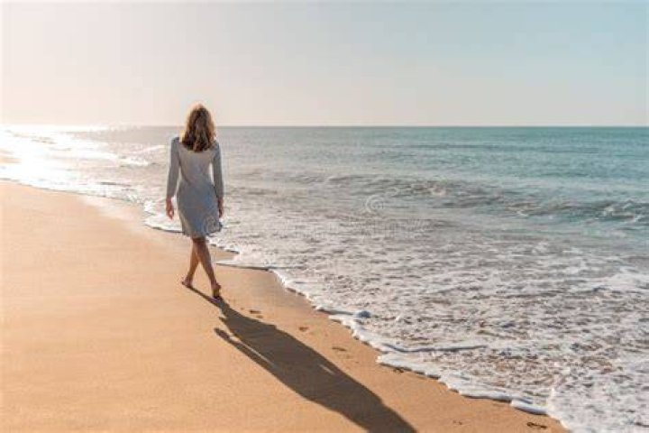 Woman walking along the beach at sunset wearing a chic flowy dress